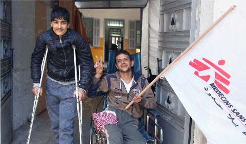 목발을 짚고 있는 환자와, 휠체어를 타고 있는 환자가 국경없는의사회 깃발을 들고 있는 모습
